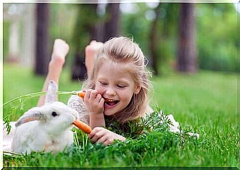 Little girl eating carrots with a rabbit.